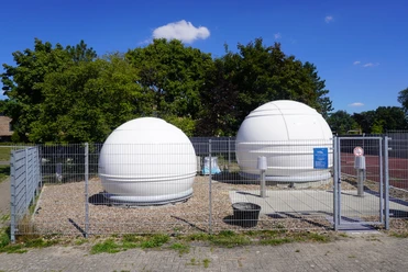 Two white domes of an observatory behind a wire fence under a clear blue sky.
