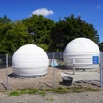 Zwei weiße Kuppeln einer Sternwarte hinter einem Drahtzaun unter einem klaren blauen Himmel.Two white domes of an observatory behind a wire fence under a clear blue sky.To hvide kupler på et observatorium bag et trådhegn under en klar blå himmel.Twee witte koepels van een observatorium achter een draadhek onder een strakblauwe hemel.