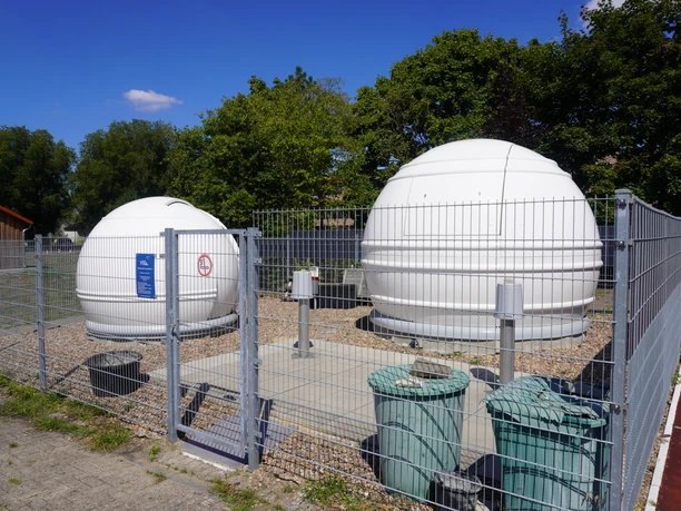 Two white domes of an observatory on a fenced-in area in sunny weather.