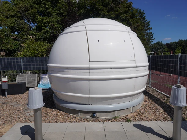 Volkssternwarte Langwedel Kuppel på Langwedel offentlige observatorium lavet af hvidt materiale, indlejret i et grønt miljø.