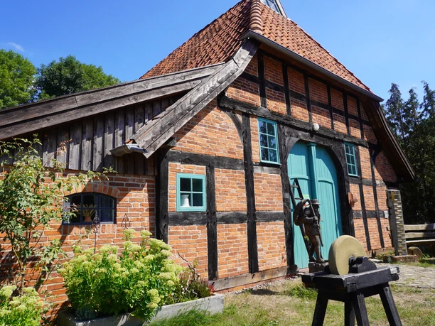 A historic half-timbered house with green arched gateways, red clinker bricks, and an idyllic cottage garden in Langwedel.