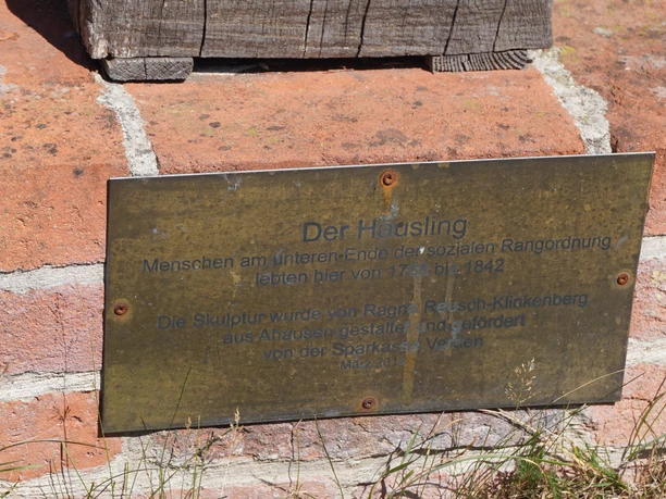 Die Tafel an einer Backsteinmauer informiert über die Skulptur "Der Häusling" von Ragnar Reusch-Klinkenberg.