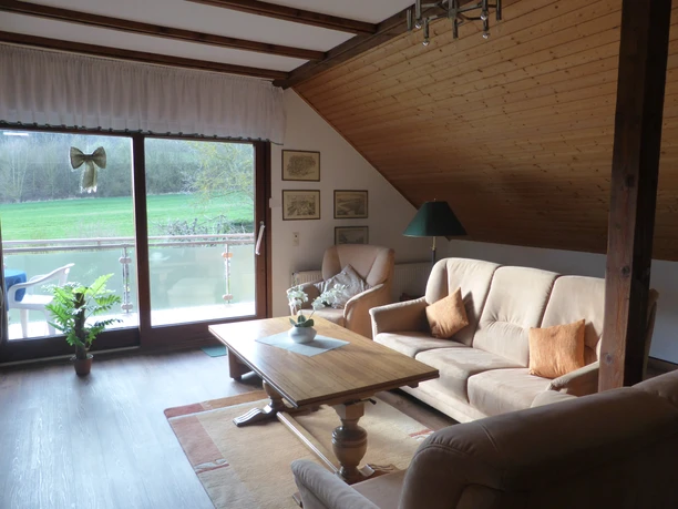 Wohnzimmer der Ferienwohnung Brigitta Hachmeyer Stilvolles Wohnzimmer in Beige mit gemütlichem Sofa und Sessel, großem Tisch und Zugang zum Balkon.