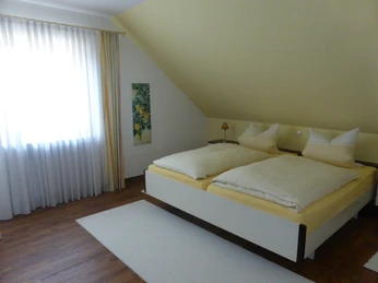 Schlafzimmer Gemütliches, helles Schlafzimmer mit Dachschräge, weißen Vorhängen und einem Doppelbett.