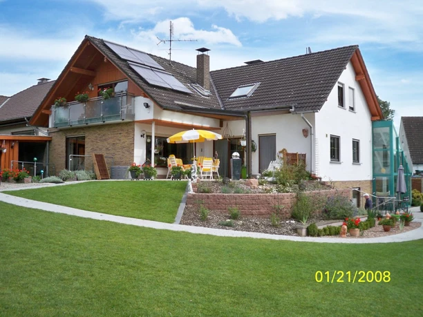 Modernes, zweistöckiges Haus mit Balkon und Terrasse, Sonnenkollektoren und gepflegter Gartenanlage.