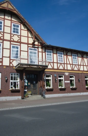 Außen.jpg Traditionelles Fachwerkhaus mit Backstein-Erdgeschoss an einer Straße unter blauem Himmel.