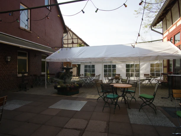 Biertuin in de geplaveide binnenplaats met zitjes, een witte tent, een fontein en een lichtslinger.