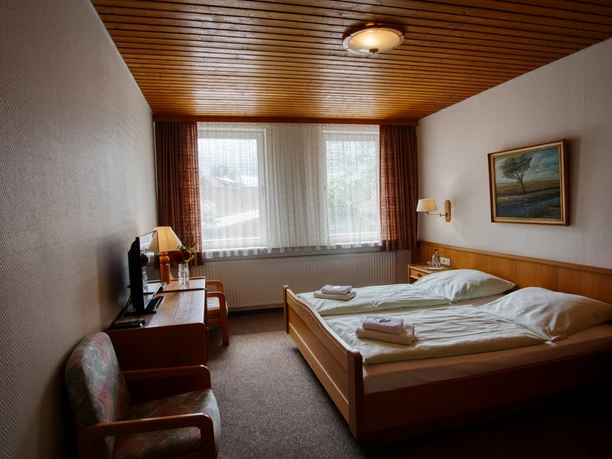Tweepersoonskamer met houten plafond, tweepersoonsbed, televisie op het dressoir en een fauteuil.