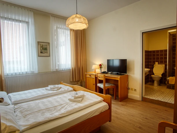 Helles Doppelzimmer mit Holzmöbeln, Schreibtisch, Fernseher und angrenzendem Badezimmer.