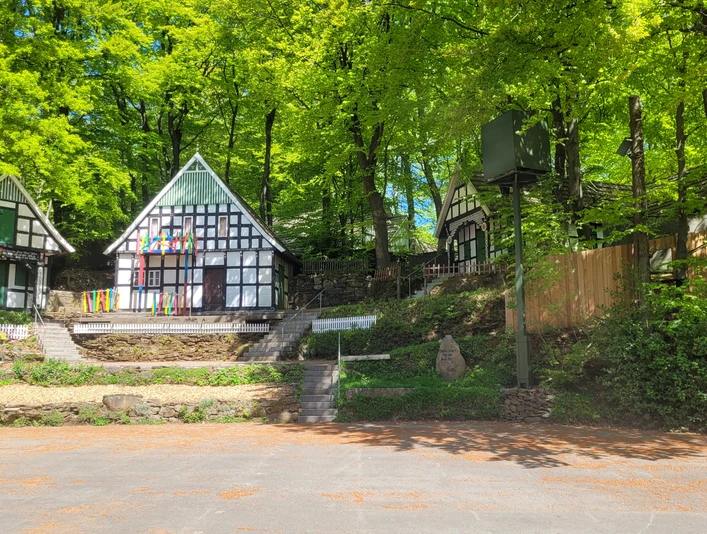 Dreieckige, von Bäumen umgebene Fachwerkhäuser bilden eine malerische Kulisse auf der Freilichtbühne.
