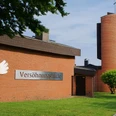 Versöhnungskirche mit rotem Backstein, grüner Wiese und Turm im Hintergrund unter blauem Himmel.