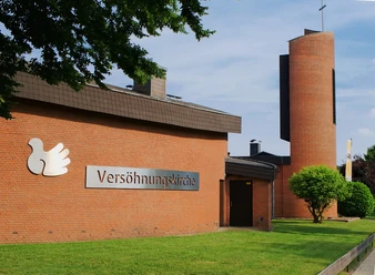 Versoehnungskirche_SHS_CC-BY-SA_Teutoburger_Wald_Stadt_Schloss_Holte-Stukenbrock_GBrauckmann.jpg Versöhnungskirche mit rotem Backstein, grüner Wiese und Turm im Hintergrund unter blauem Himmel.