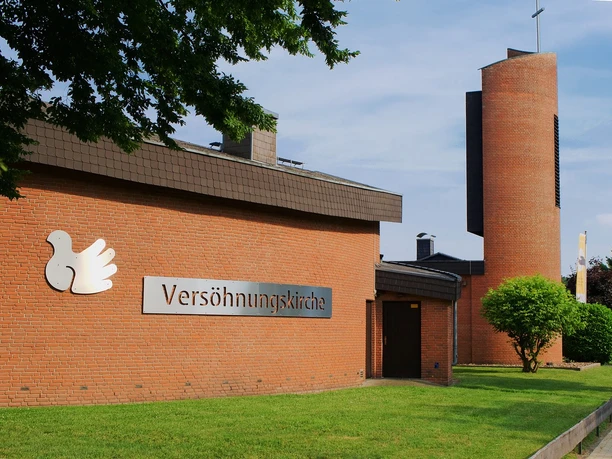 Versoehnungskirche_SHS_CC-BY-SA_Teutoburger_Wald_Stadt_Schloss_Holte-Stukenbrock_GBrauckmann.jpg Versöhnungskirche mit rotem Backstein, grüner Wiese und Turm im Hintergrund unter blauem Himmel.