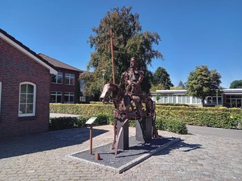 Lieblingsort Rathausmarkt Apen mit Ritter Herbord Eine imposante Metallskulptur eines Ritters auf einem Metallpferd steht auf gepflastertem Platz vor Büschen und Gebäuden, umgeben von klarem Himmel an einem sonnigen Tag.