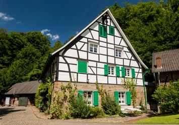 Lambertsmühle Fachwerkhaus mit grünen Fensterläden, umgeben von Natur und blauem Himmel in Burscheid.