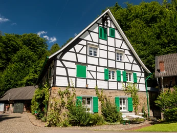 Lambertsmühle Fachwerkhaus mit grünen Fensterläden, umgeben von Natur und blauem Himmel in Burscheid.