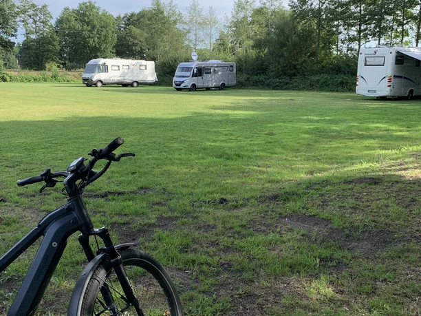 Stellplatz am Freibad Hengstforde Grüne Wiese mit drei parkenden Wohnmobilen und einem Fahrrad im Vordergrund .