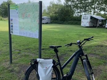 Wohnmobilstellplatz am Freibad Hengstforde Das Bild zeigt einen Wohnmobilstellplatz neben einem grünen Wiesengelände mit einem Fahrrad im Vordergrund und Wohnmobilen im Hintergrund. Ein Informationsschild bietet den Besuchern relevante Details zur Umgebung.