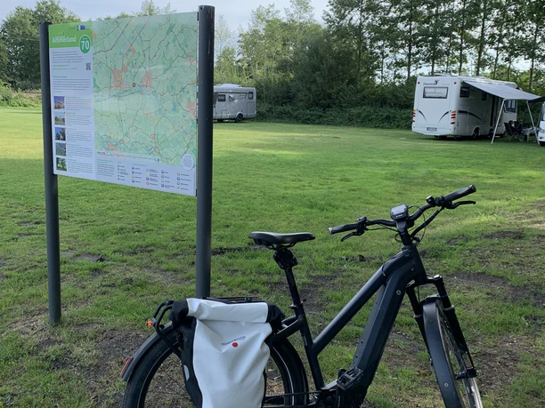Wohnmobilstellplatz am Freibad Hengstforde Das Bild zeigt einen Wohnmobilstellplatz neben einem grünen Wiesengelände mit einem Fahrrad im Vordergrund und Wohnmobilen im Hintergrund. Ein Informationsschild bietet den Besuchern relevante Details zur Umgebung.