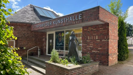 Ingang van de Worpswede Kunsthalle, een rood bakstenen gebouw met een beeld van een vrouw naast de ingang