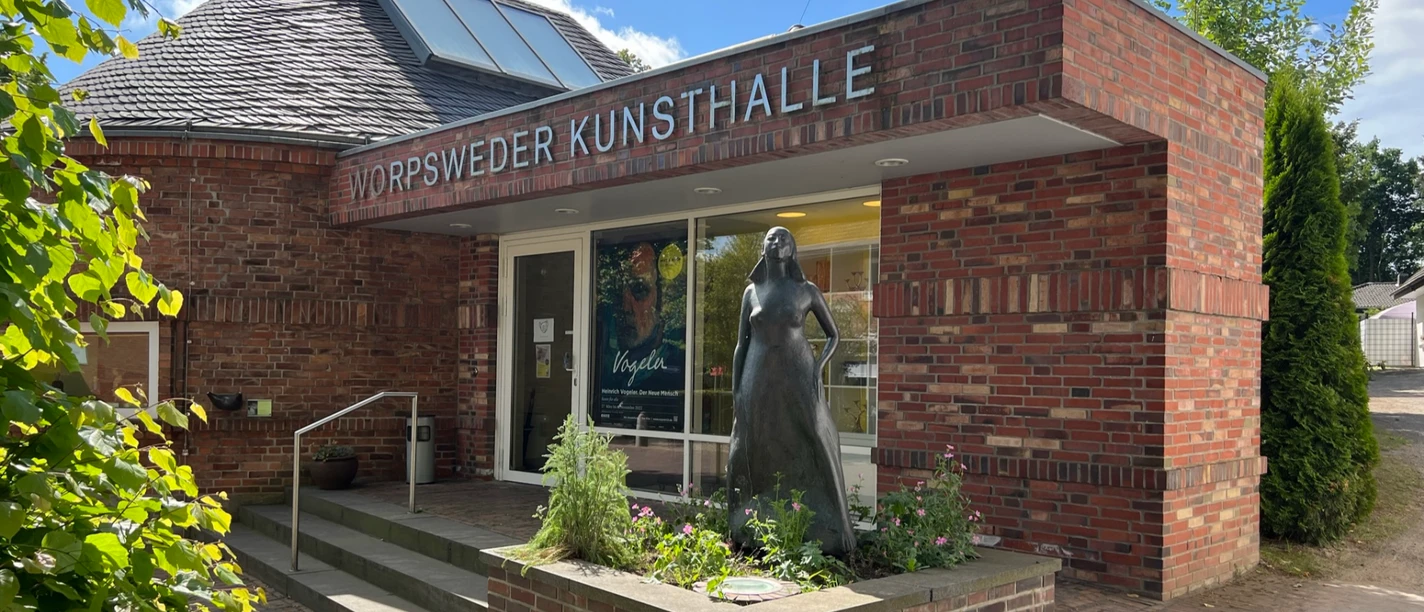 Ingang van de Worpswede Kunsthalle, een rood bakstenen gebouw met een beeld van een vrouw naast de ingang