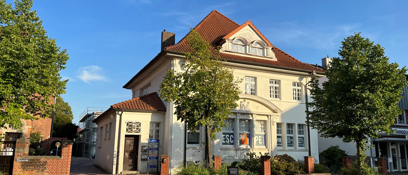 Escape Room A large, white building with a red roof and escape room signs on the façade, surrounded by trees.