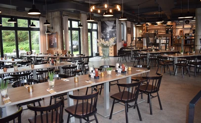 Restaurant Zur Gießerei im Best Western plus Parkhotel Velbert Restaurant mit modernen Holztischen und dunklen Stühlen, umgeben von großen Fenstern und stilvoller Beleuchtung.