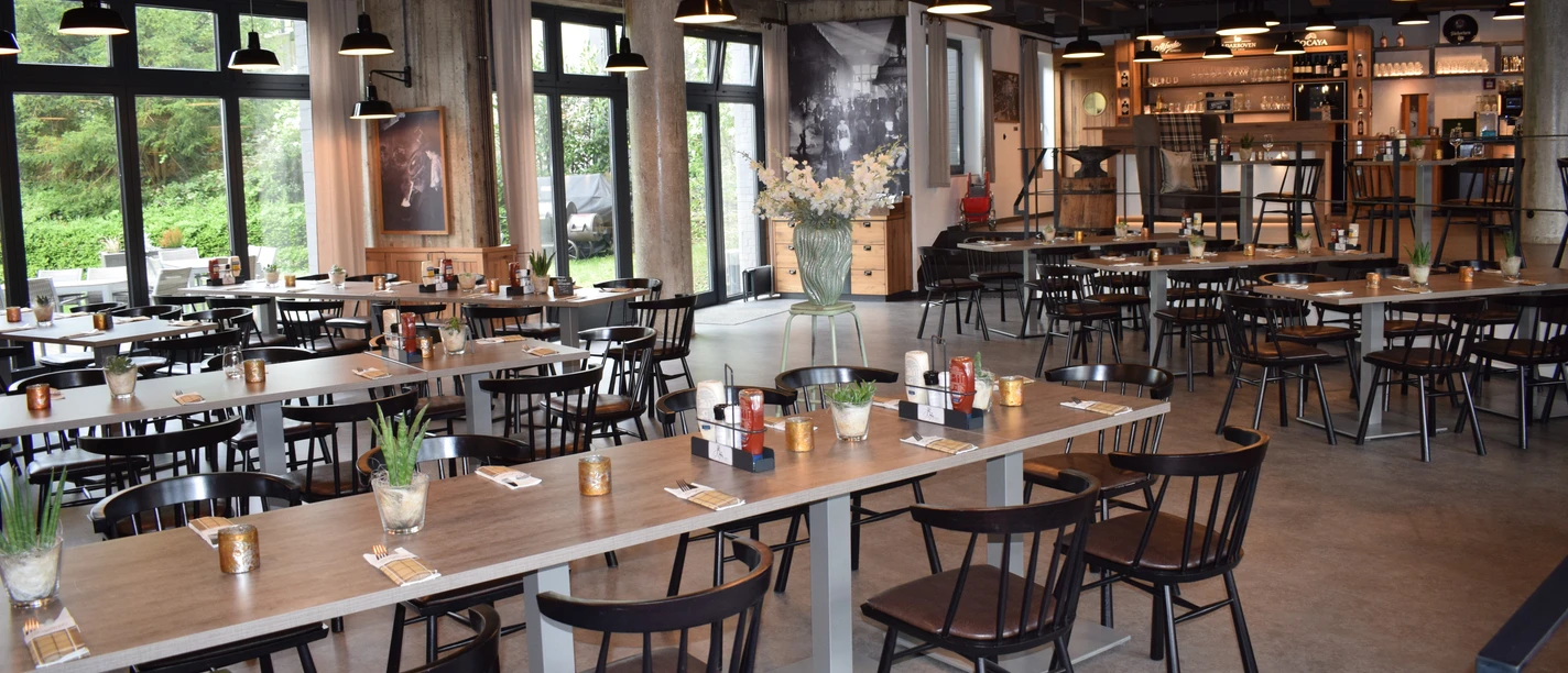 Restaurant Zur Gießerei im Best Western plus Parkhotel Velbert Restaurant mit modernen Holztischen und dunklen Stühlen, umgeben von großen Fenstern und stilvoller Beleuchtung.