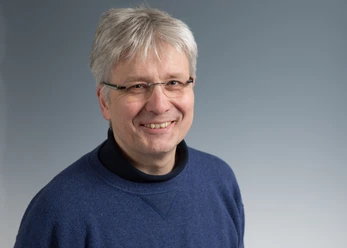 Der Domorganist Michael Hoppe, der graue kurze Haare und eine Brille trägt, lacht in die Kamera.