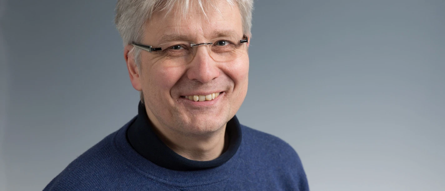 Der Domorganist Michael Hoppe, der graue kurze Haare und eine Brille trägt, lacht in die Kamera.