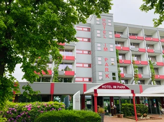 Hotel IM PARK in Bad Iburg, modernes mehrstöckiges Gebäude mit rot-weißen Balkonen und grünem Umfeld.