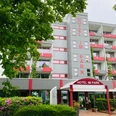 Hotel IM PARK, Bad Iburg Hotel IM PARK in Bad Iburg, modernes mehrstöckiges Gebäude mit rot-weißen Balkonen und grünem Umfeld.