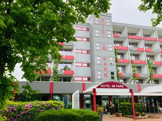 Hotel IM PARK, Bad Iburg Hotel IM PARK in Bad Iburg, modernes mehrstöckiges Gebäude mit rot-weißen Balkonen und grünem Umfeld.