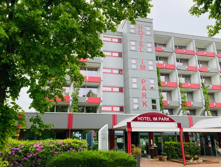 Hotel IM PARK, Bad Iburg Hotel IM PARK in Bad Iburg, modernes mehrstöckiges Gebäude mit rot-weißen Balkonen und grünem Umfeld.