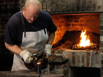 Schmiedevorführung Ein Schmied arbeitet konzentriert an einem Stück Metall, während im Hintergrund das Feuer lodert.