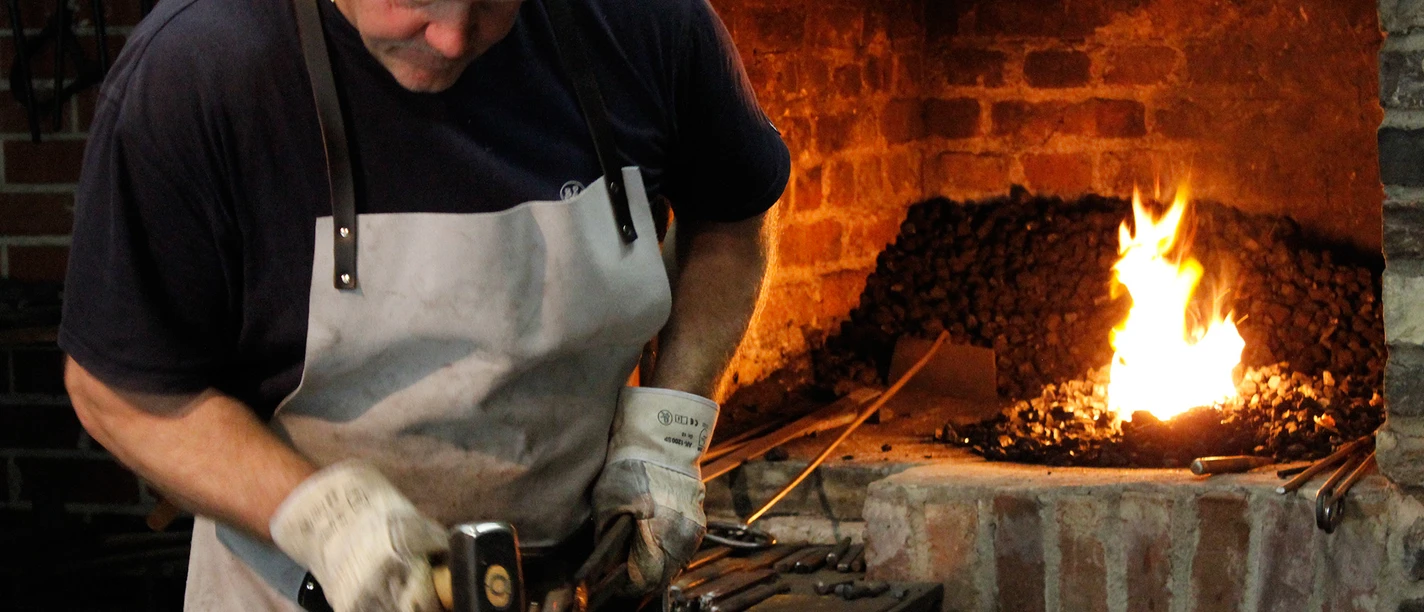 Schmiedevorführung Ein Schmied arbeitet konzentriert an einem Stück Metall, während im Hintergrund das Feuer lodert.