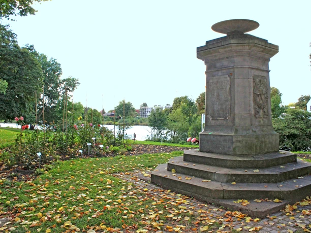Steinmonument am Weserwall, umgeben von Herbstlaub und Bäumen in einer friedlichen Parklandschaft.
