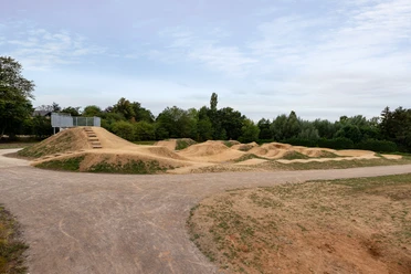 Dirt-Bike-Anlage Fernholz, Ratingen Weitläufige Dirt-Bike-Strecke mit Erdhügeln und Kurven, umgeben von Bäumen und freiem Himmel.