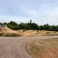 Dirt-Bike-Anlage Fernholz, Ratingen Weitläufige Dirt-Bike-Strecke mit Erdhügeln und Kurven, umgeben von Bäumen und freiem Himmel.