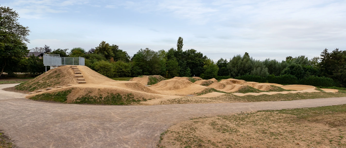 Dirt-Bike-Anlage Fernholz, Ratingen Weitläufige Dirt-Bike-Strecke mit Erdhügeln und Kurven, umgeben von Bäumen und freiem Himmel.