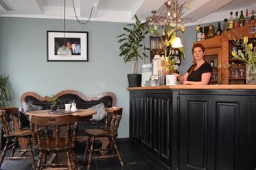 Café am Markt in Mettmann Einladendes Café mit Holzmöbeln, Bar, Wanddekoration und blühenden Pflanzen im Inneren.