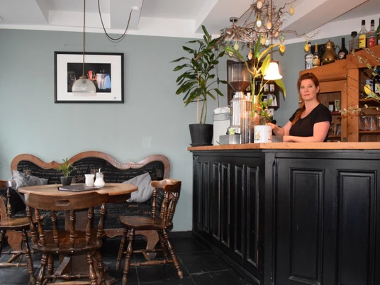 Café am Markt in Mettmann Einladendes Café mit Holzmöbeln, Bar, Wanddekoration und blühenden Pflanzen im Inneren.