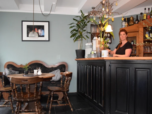 Café am Markt in Mettmann Einladendes Café mit Holzmöbeln, Bar, Wanddekoration und blühenden Pflanzen im Inneren.