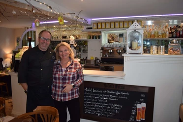 Inhaber des Restaurants La Pieve in Mettmann Ein lächelndes Paar steht in einem gemütlichen Restaurant vor einer Tafel mit Menüangeboten.