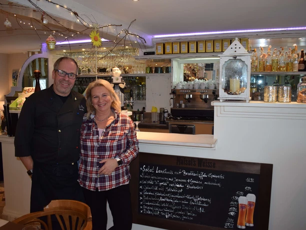 Inhaber des Restaurants La Pieve in Mettmann Ein lächelndes Paar steht in einem gemütlichen Restaurant vor einer Tafel mit Menüangeboten.