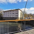 Neues Baumwolllager Ansicht eines historischen weißen Gebäudes an einem Fluss, mit moderner Brücke im Vordergrund.