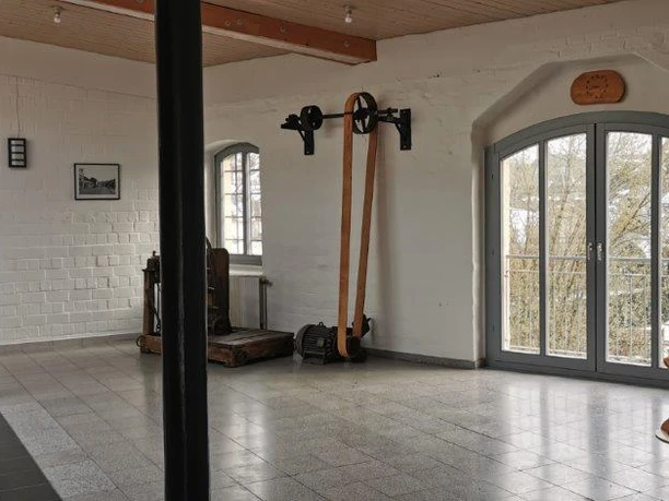 Innenansicht Heller Raum mit Blick ins Freie, alten Turngeräten an der Wand und einem Klavier rechts im Bild.