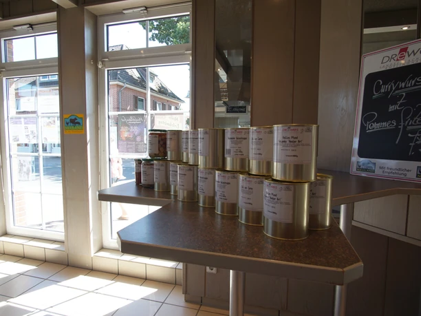Innenraum-total 2.jpg Innenbereich eines Bistros mit gestapelten Dosen lokaler Fleischspezialitäten auf einem Stehtisch.