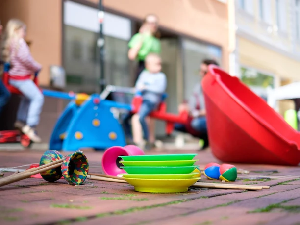 Farbenfrohe Spielgeräte und Kinder beim Weltkindertag, im Vordergrund jonglierbälle und Teller.