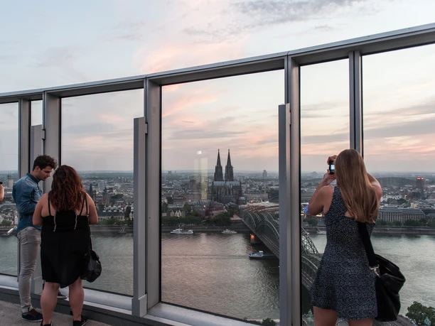 KölnTriangle Visitors enjoy the breathtaking view from the viewing platform of the KölnTriangle over the city of Cologne, which shines in the evening light. The panoramic view includes the majestic Cologne Cathedral and the glittering Rhine landscape, offering an unforgettable experience.